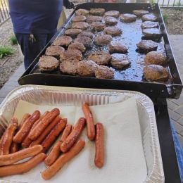 hot dogs in a foil pan and hamburgers on a grill